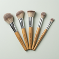 Set of six wooden makeup brushes with silver ferrules on a light gray background